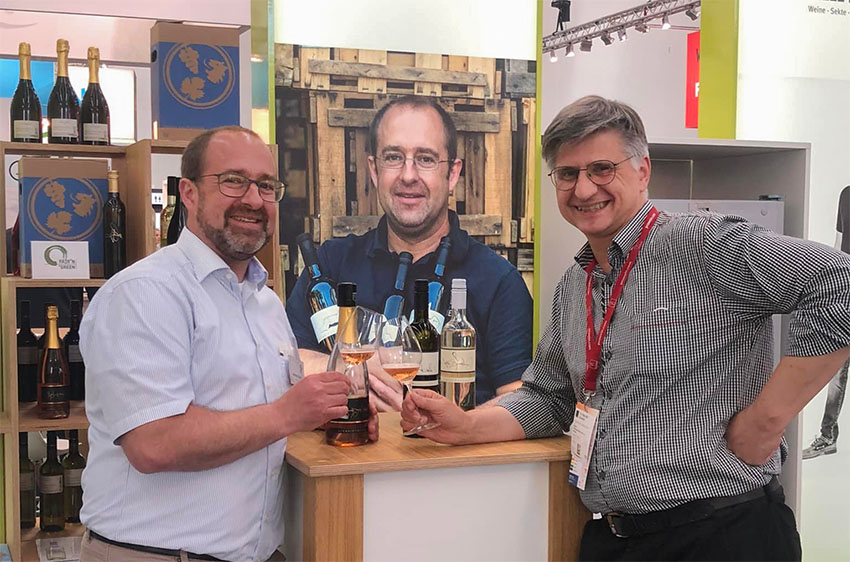 Zwei Männer mit Weingläsern in der Hand vor einem Weinstand