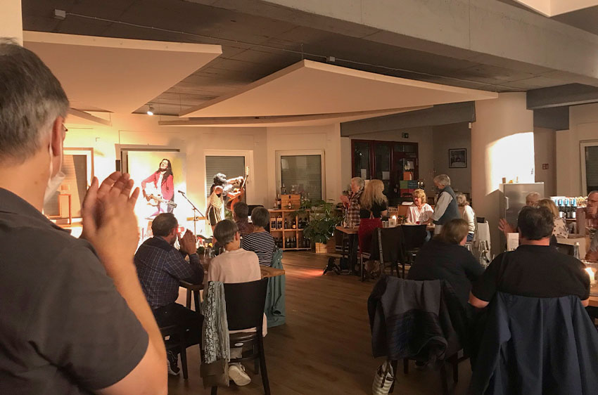 Eine kleine Bühne mit Künstlerin in einem Weinlokal mit viel Publikum an Tischen