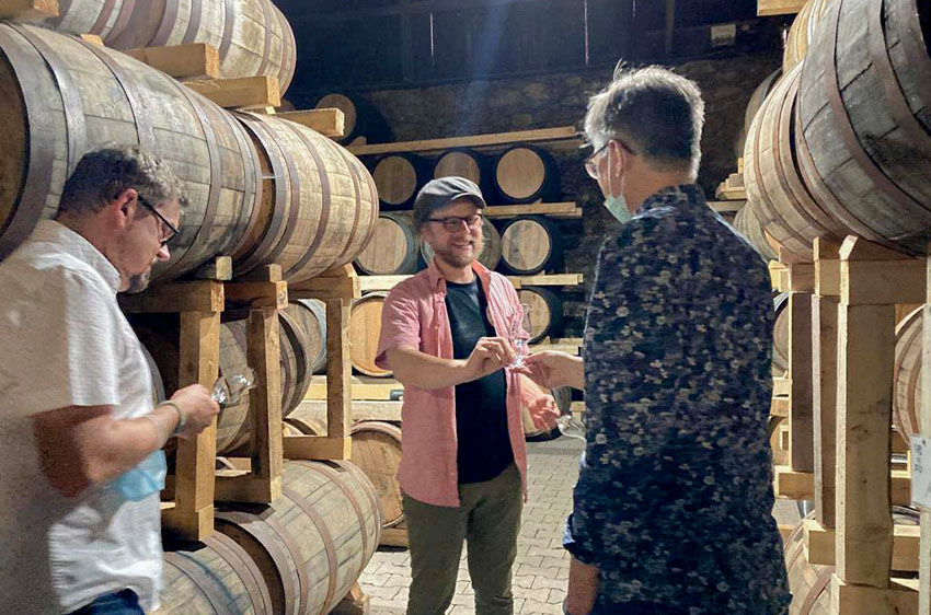 Zwei Männer in einem Keller voller Holzfässer mit Gläsern in der Hand